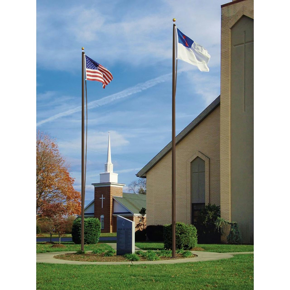 A tall aluminum flagpole with a gold anodized ball on top, displaying two flags, installed outside near a church.