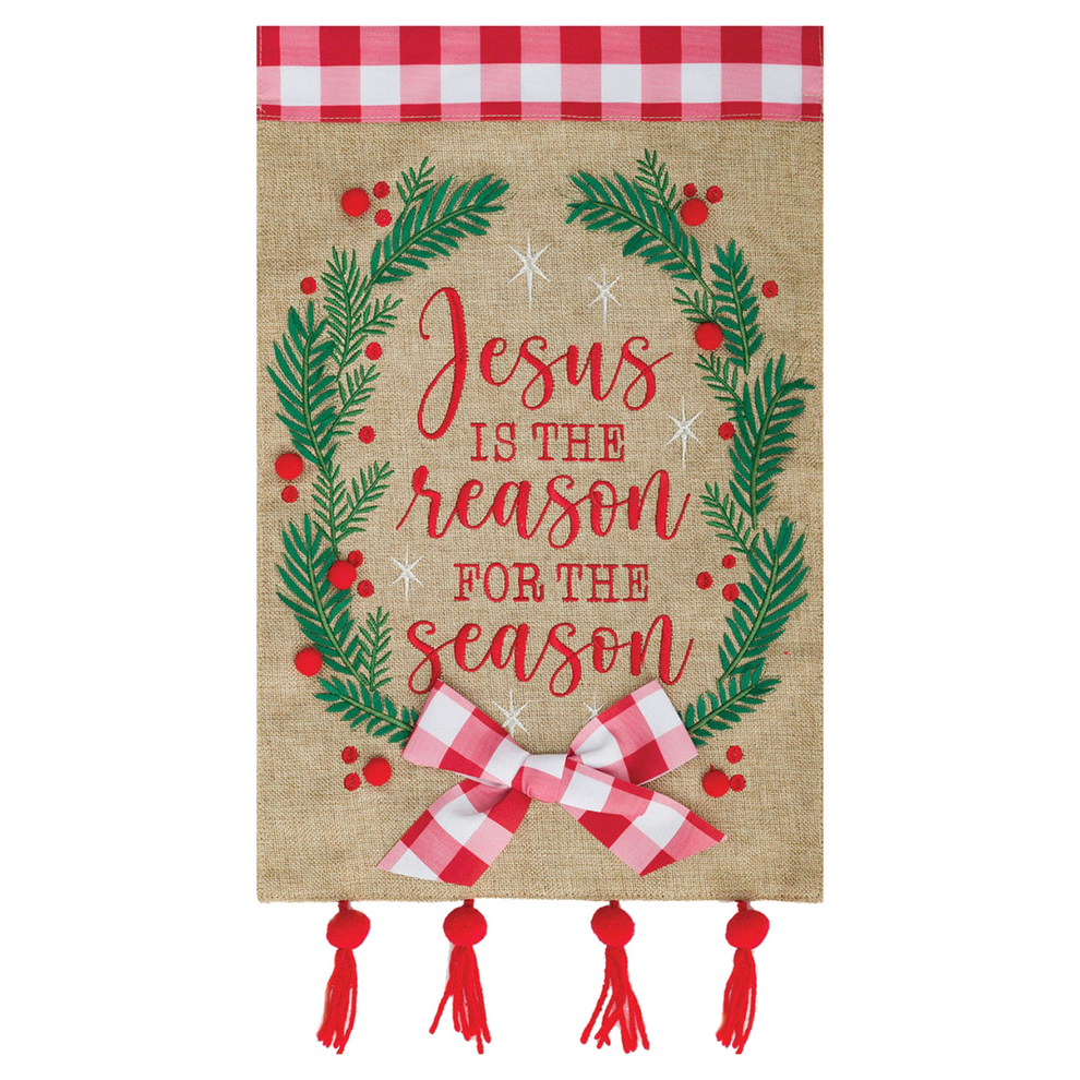 Decorative garden flag banner with 'Jesus is the reason for the season' text, surrounded by greenery and a bow on a burlap background.