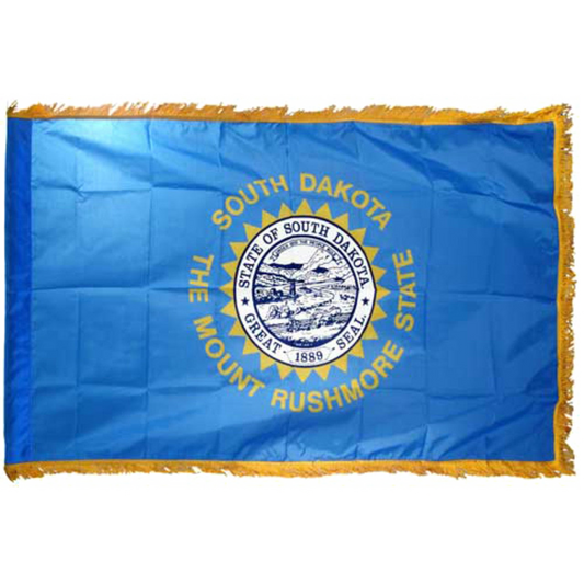 State of South Dakota state flag featuring the full-color state seal, gold sunburst, and 'South Dakota, The Mount Rushmore State' text on a solid sky-blue field. Flag has fringe on the edges