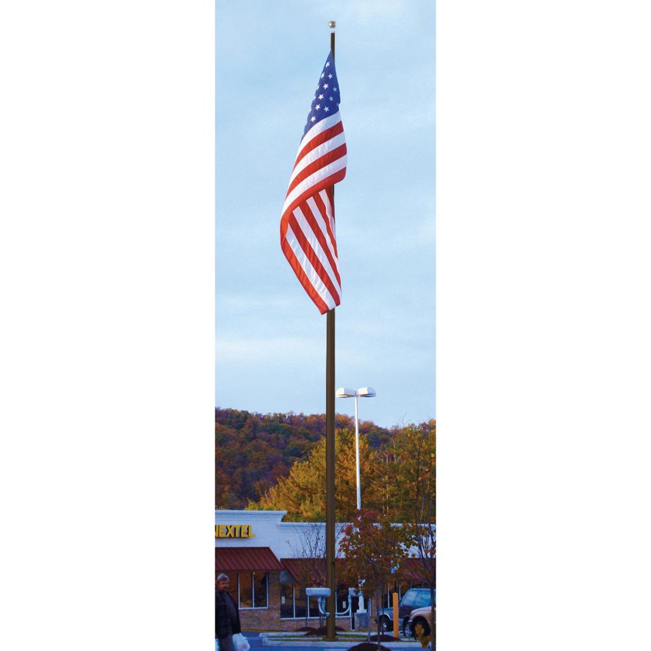 A large American flag on a large commercial flagpole in a parking lot with built-ins and trees in the background.