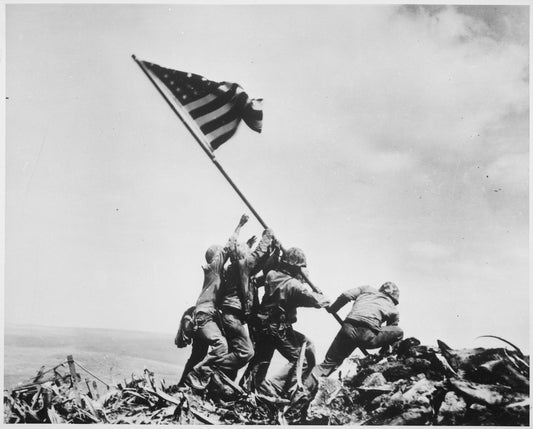 Official black and white image of the flag being raised on Iwo Jima by 6 Marines using their bodies to hoist the flag and flagpole