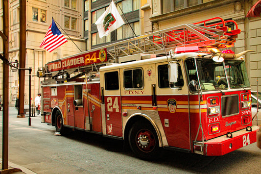 A red and cream New York City Fire Department (FDNY) Engine 24 fire truck parked on a city street, with its ladder extended, an American flag, and a FDNY flag hanging above it.