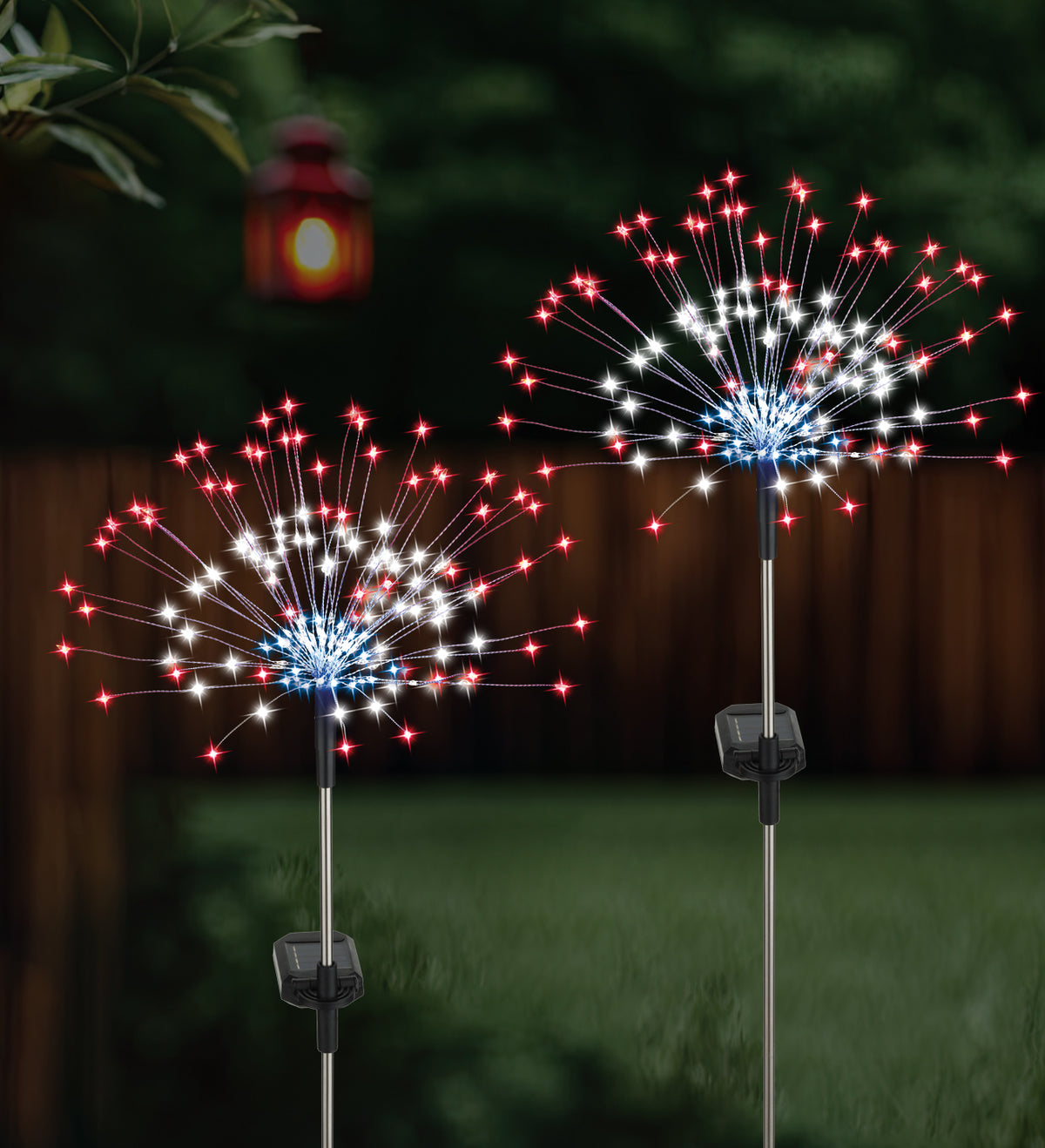 Two solar-powered outdoor light fixtures shaped like fireworks on a grassy area with a lantern in the background.