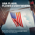 A premium heavyweight American flag flying majestically between city buildings against a cloudy sky.