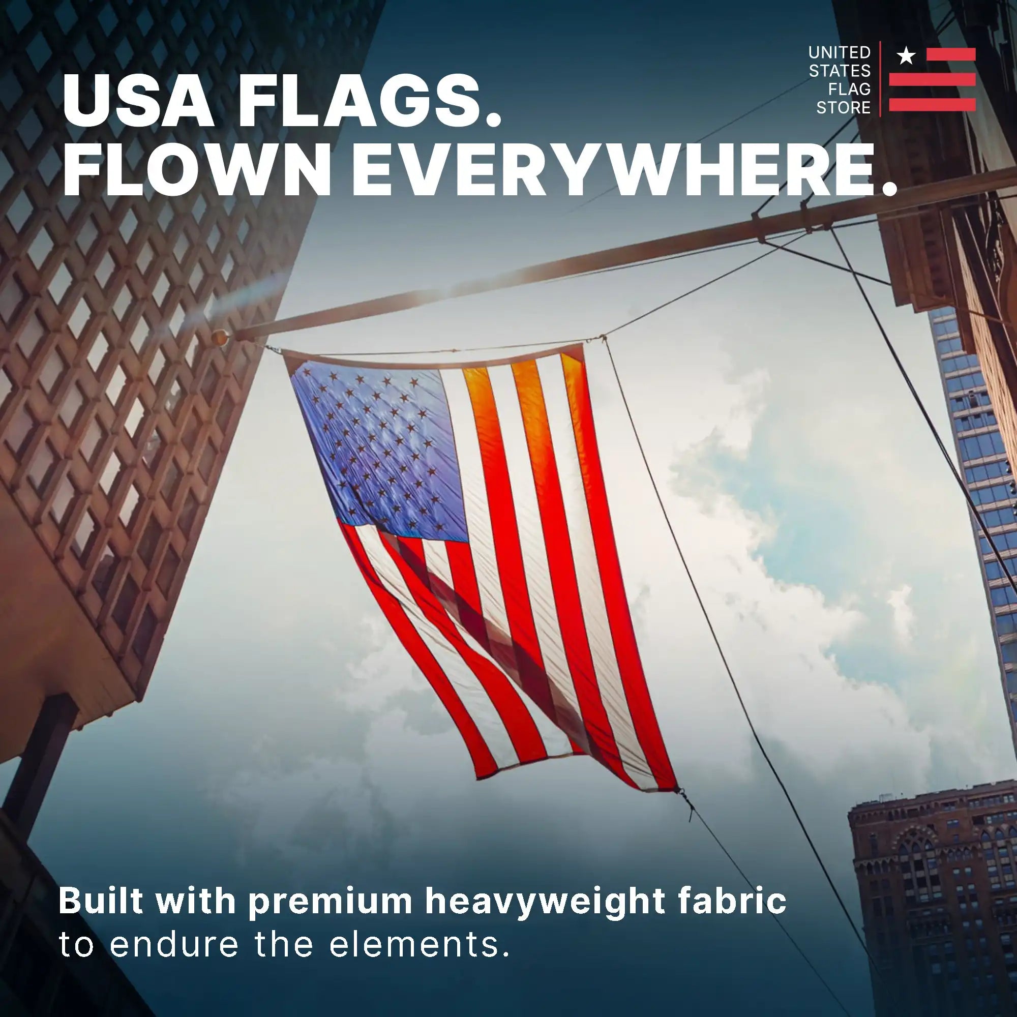 A premium heavyweight American flag flying majestically between city buildings against a cloudy sky.