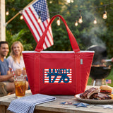 Red cooler bag with 4th of July design on a table with food and people in the background.