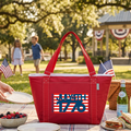 Red cooler bag with 'July 4th 1776' design on a picnic table with people and flags in the background.