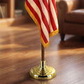 Close-up of an indoor flagpole set showing a gold base, wooden pole, and fringed flag.