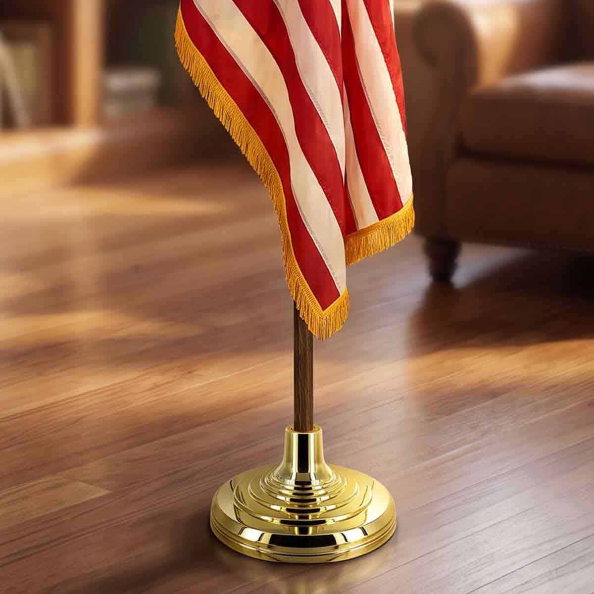 Close-up of an indoor flagpole set showing a gold base, wooden pole, and fringed flag.