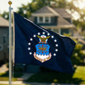 Navy blue flag with an emblem featuring an eagle and stars, waving in front of a blurred house and trees.