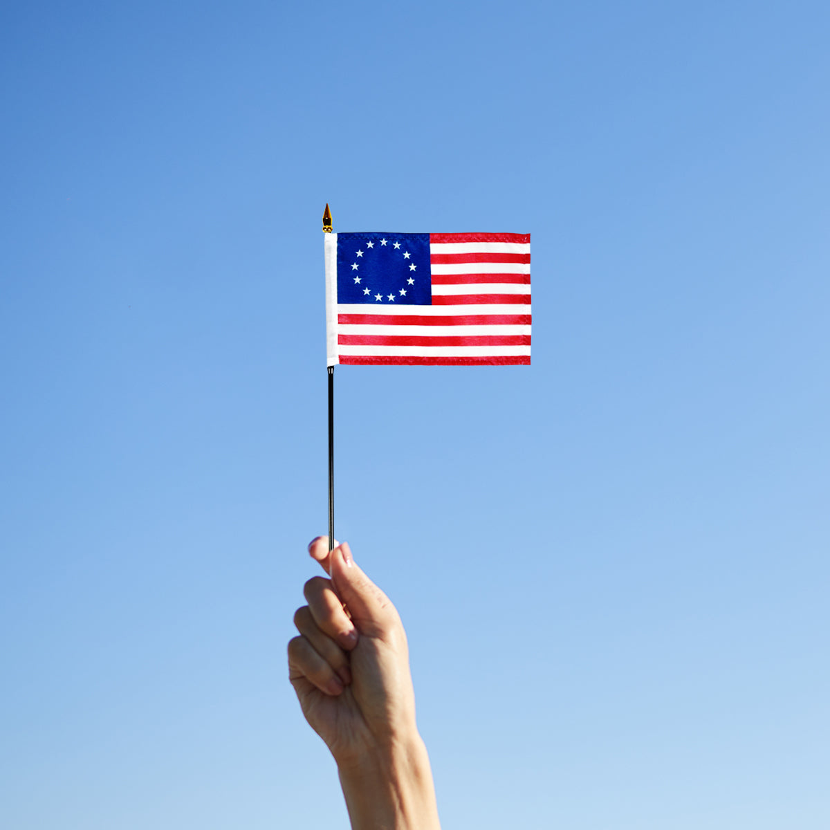 Hand holding a small Betsy Ross American flag against a clear blue sky