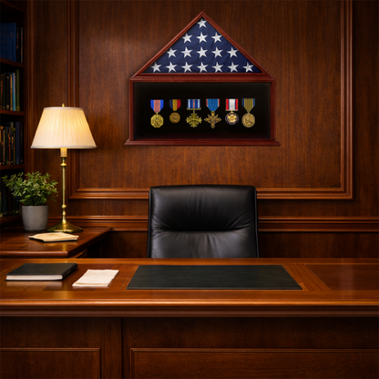 Wooden office desk with black leather chair, lamp, and framed American flag with medals on a wooden wall.