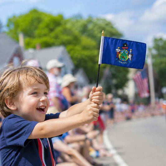 Child waving a Maine state hand flag at a summer parade