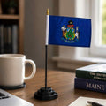 Maine state flag on a desk stand next to a coffee mug and books