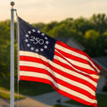 American flag with '250' in the center of 13 stars in a circle in the blue cantor of the flag as the sun is setting creating a glow.