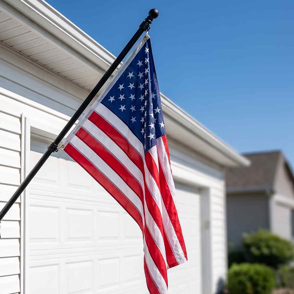 Black residential flagpole with American flag mounted beside a white garage