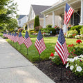 Small American flags on garden stakes along a suburban sidewalk, patriotic yard decor for Memorial Day and Fourth of July