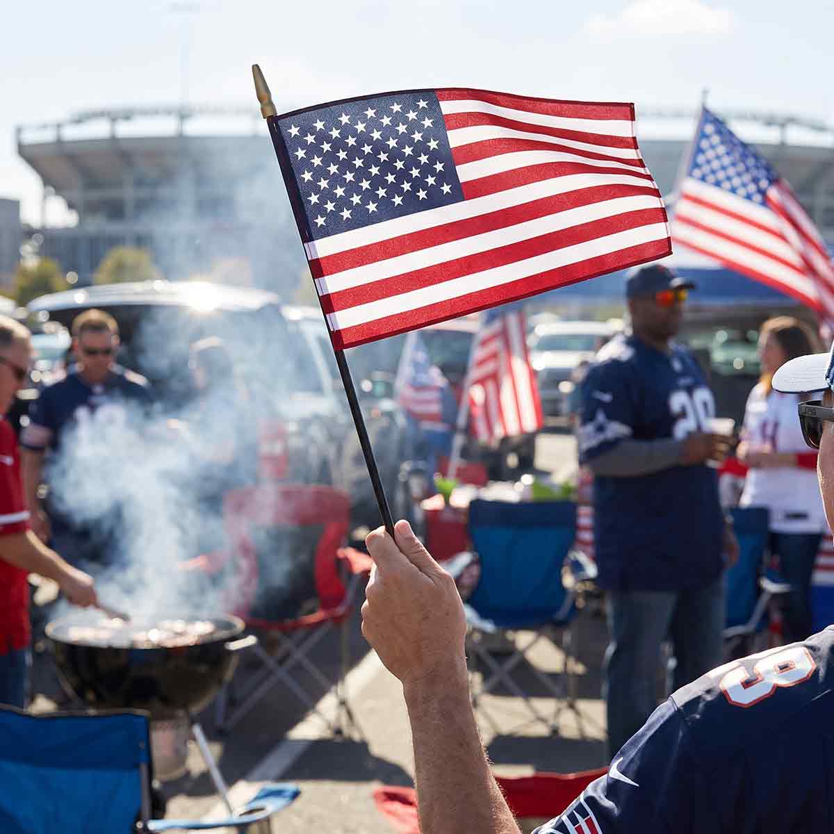Small American stick flag held at a tailgate party outside a stadium, patriotic hand flag for sports events and outdoor celebrations
