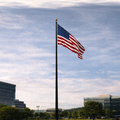 American flag on a flagpole against a cloudy sky with buildings and trees in the background