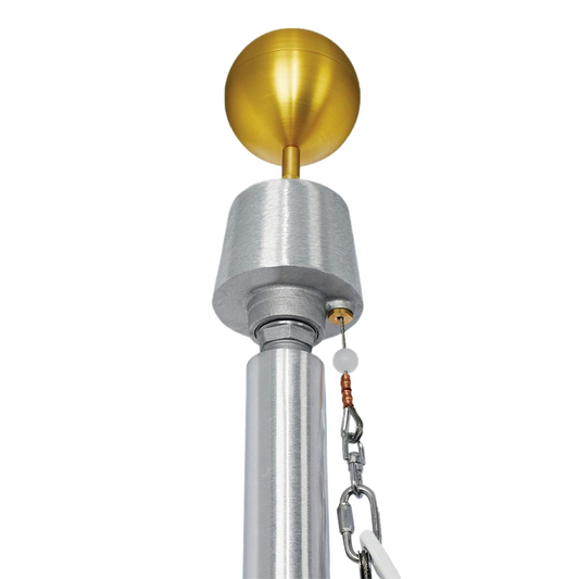 Close up of a gold ball flagpole topper on top of a metal flagpole with a rope pulley system and rope with the top of a flag.