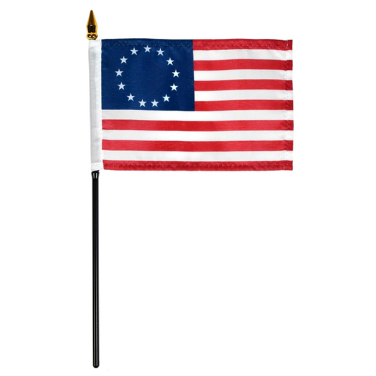 Betsy Ross style American flag with 13 stars in a circle on a blue canton and red and white stripes, mounted on a black stick with a gold spear finial, isolated on a white background.