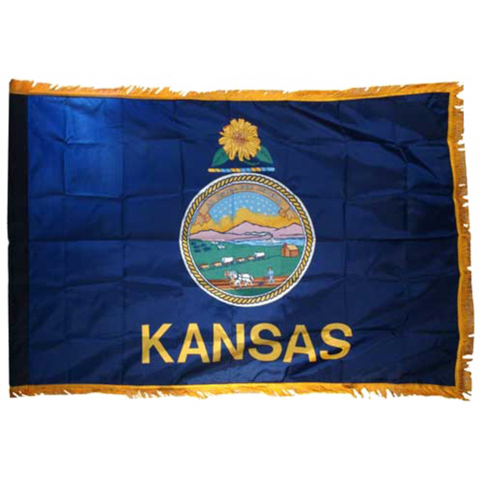 State of Kansas blue flag with Kansas state seal in the center, depicting a landscape with a rising sun, a steamship, a settler plowing a field, a covered wagon train, and Native Americans hunting buffalo. Above the scenery is the Latin motto 'AD ASTRA PER ASPERA'. Above the seal sits a gold and blue sunflower twist, and the word 'KANSAS' is printed in large, gold all-caps letters directly below the seal.  Flag features yellow fringe.
