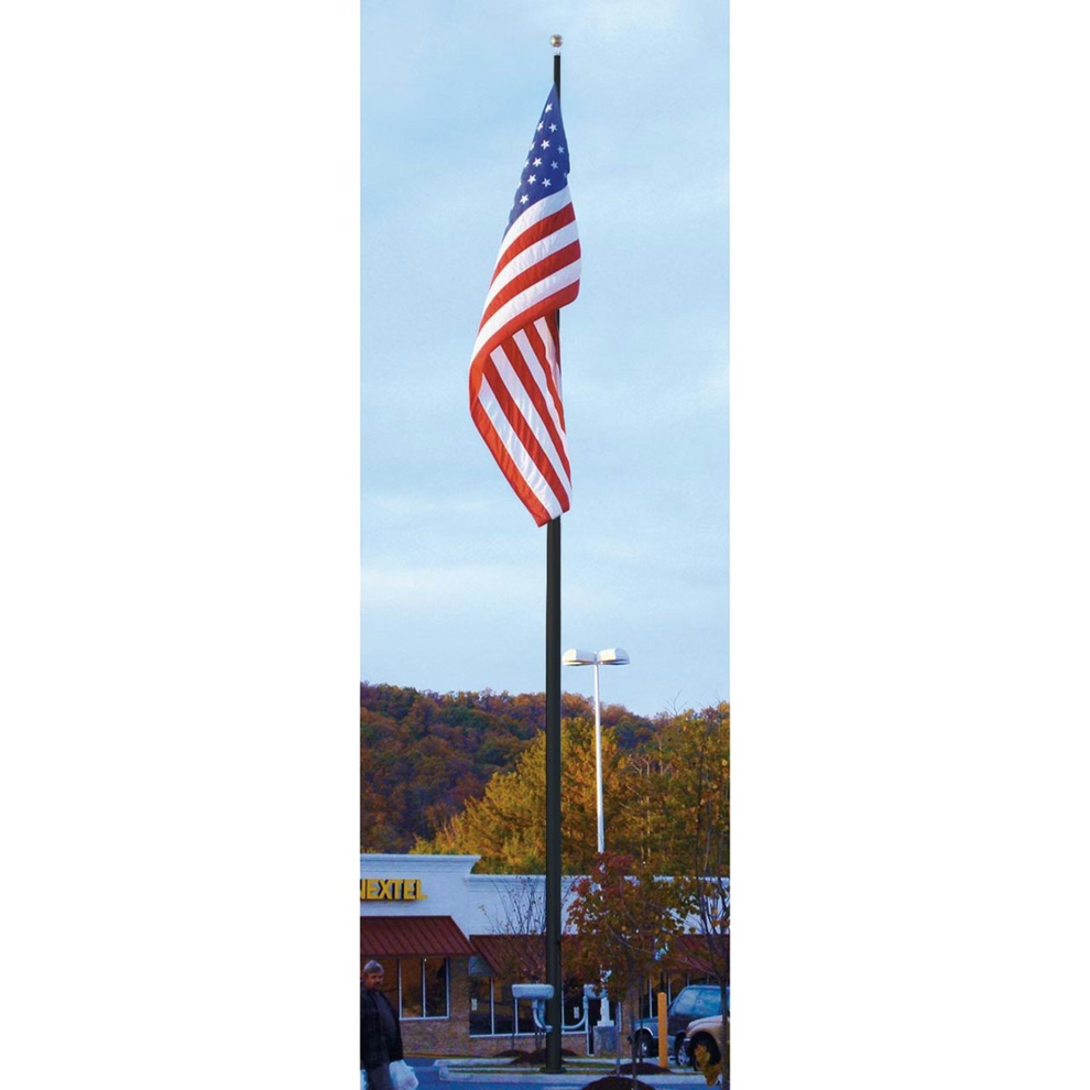 A large American flag on a large commercial flagpole in a parking lot with built-ins and trees in the background.