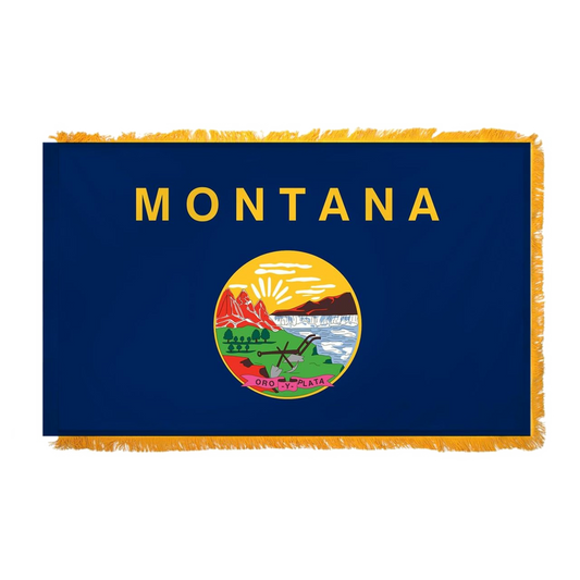 State of Montana flag with 'MONTANA' printed in large, gold all-caps letters across the top. Centered below the text is the full-color state seal, depicting a landscape with the Rocky Mountains, the Great Falls of the Missouri River, a plow, a shovel, and a pick. A ribbon at the bottom of the seal reads the Spanish motto 'ORO Y PLATA'.  This flag features yellow fringe.