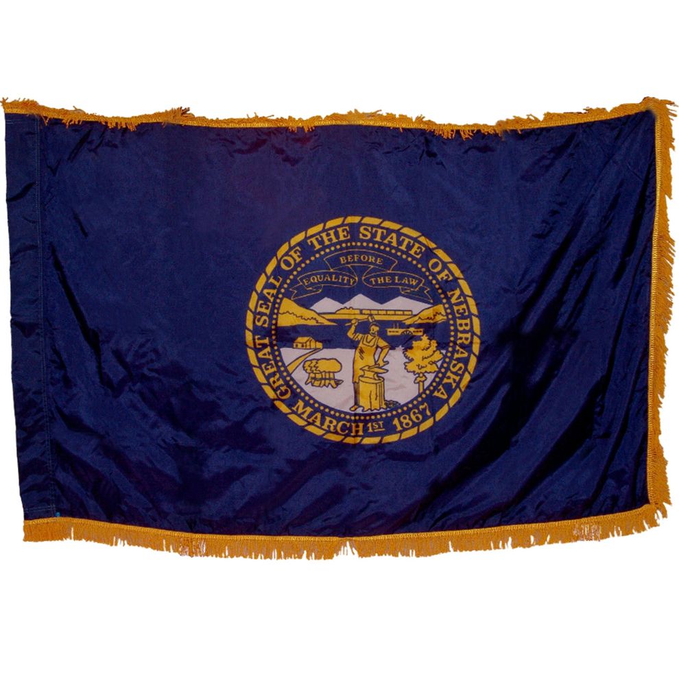 State of Nebraska state flag featuring the gold and silver state seal with the motto 'Equality Before the Law' on a solid dark blue field.  Seal includes a steamboat on a river, a train moving across mountains, a blacksmith at work, and a settler's cabin.  This flag features yellow fringe.