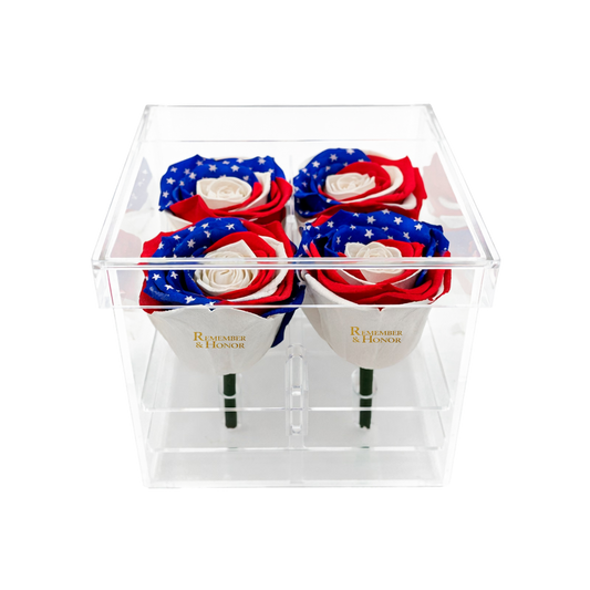 Four red, white, and blue roses in a clear box with 'Remember & Honor' branding.
