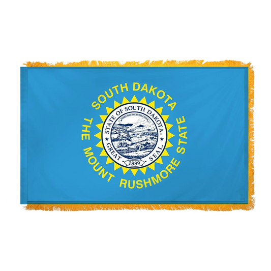 State of South Dakota state flag featuring the full-color state seal, gold sunburst, and 'South Dakota, The Mount Rushmore State' text on a solid sky-blue field.  Flag has fringe on the edges.