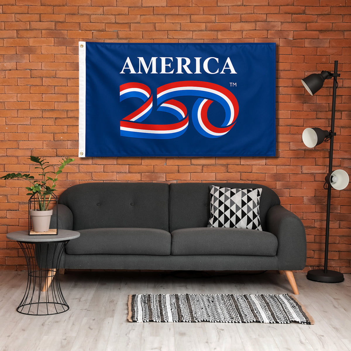 Living room with a 'America 250' flag on a brick wall, gray sofa, and decorative items.