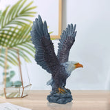 Eagle statue with open wings on a wooden surface with a blurred plant and frame in the background