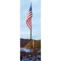 A large American flag on a large commercial flagpole in a parking lot with built-ins and trees in the background.