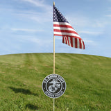 American flag on a pole with a U.S. Marine Corps sign in the foreground against a blue sky.