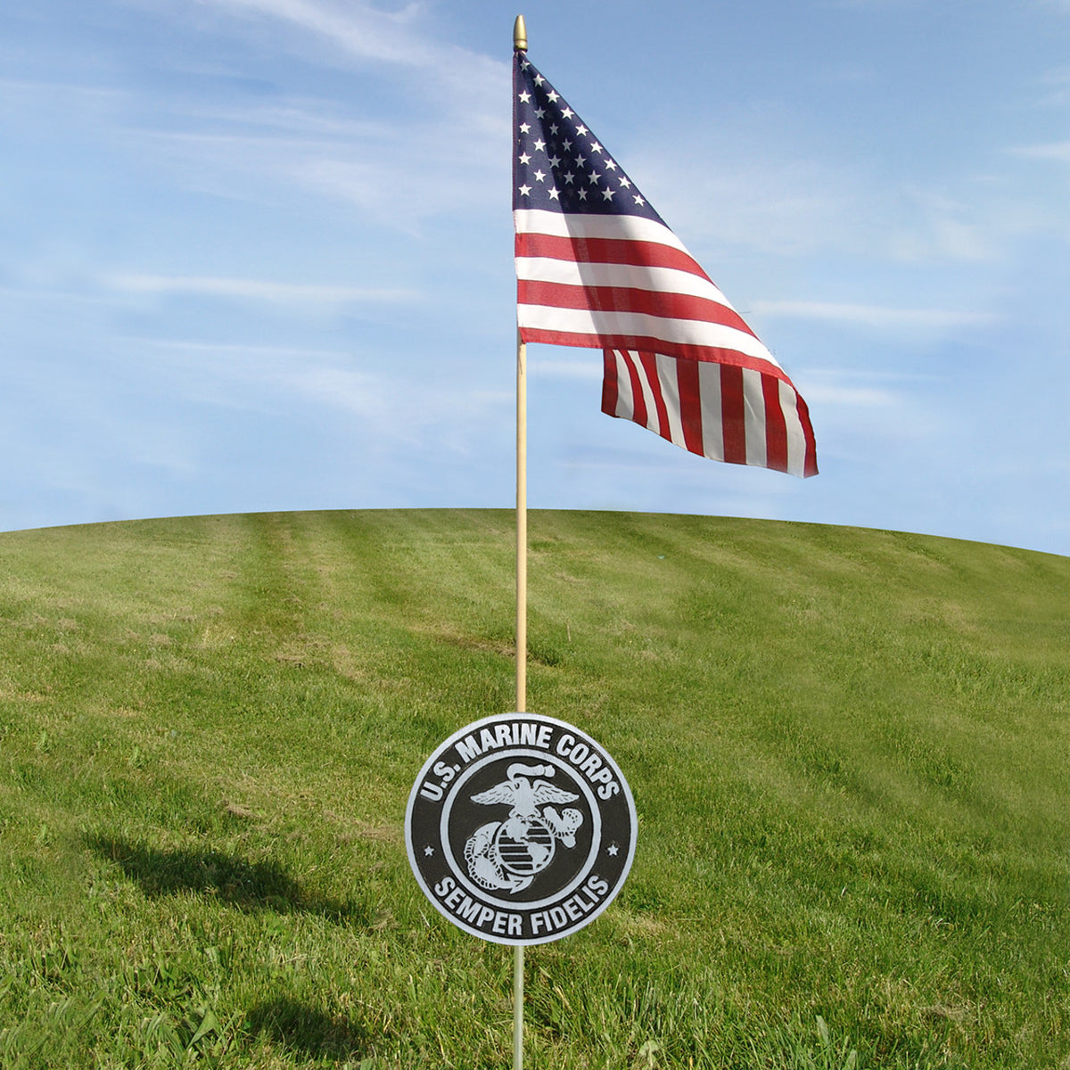 American flag on a pole with a U.S. Marine Corps sign in the foreground against a blue sky.