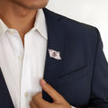 Close-up of a person wearing a dark blazer with a lapel pin and a white shirt.