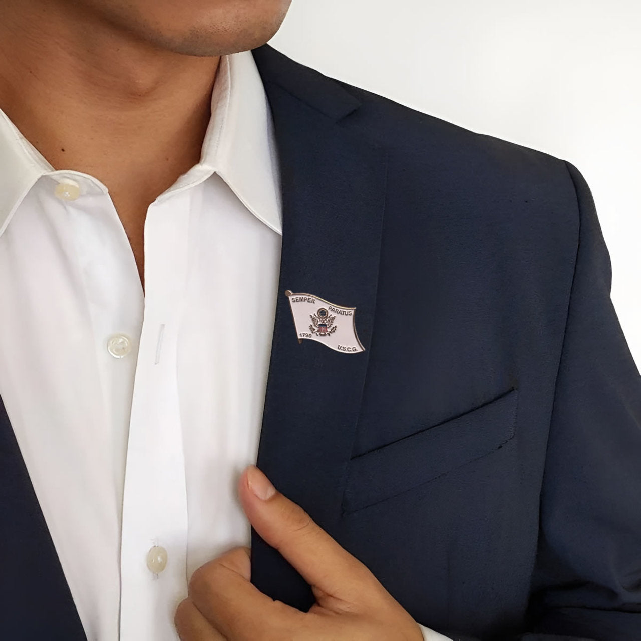 Close-up of a person wearing a dark blazer with a lapel pin and a white shirt.