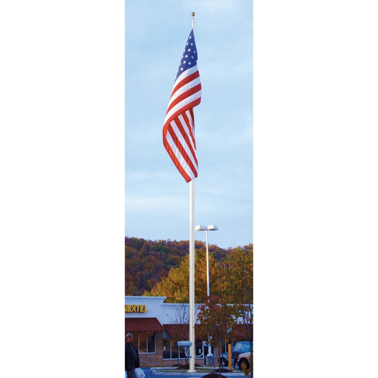 A large American flag on a large commercial flagpole in a parking lot with built-ins and trees in the background.
