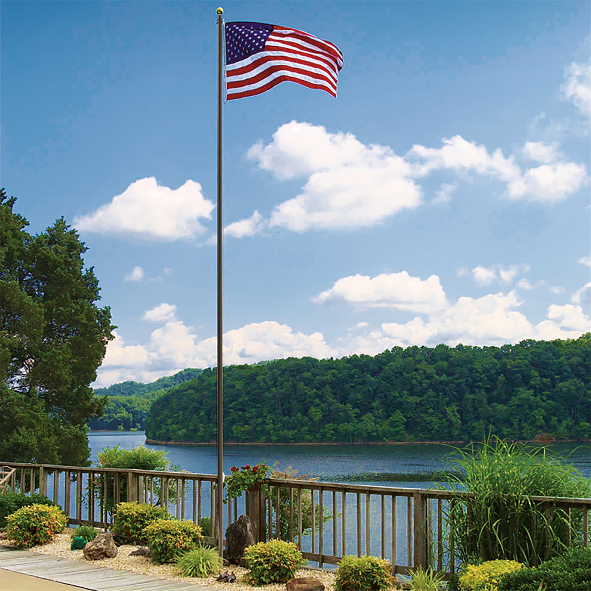 American flag waving on a flagpole with a scenic view of a lake and trees in the background.