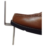 Close-up of a brown leather shoe stepping on the horizontal foot peg of a silver metal ground stake.