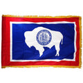 Wyoming state flag with a white silhouette of a bison and a blue background on a red field, featuring a yellow fringe border.