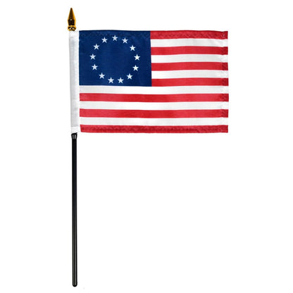 Betsy Ross style American flag with 13 stars in a circle on a blue canton and red and white stripes, mounted on a black stick with a gold spear finial, isolated on a white background.